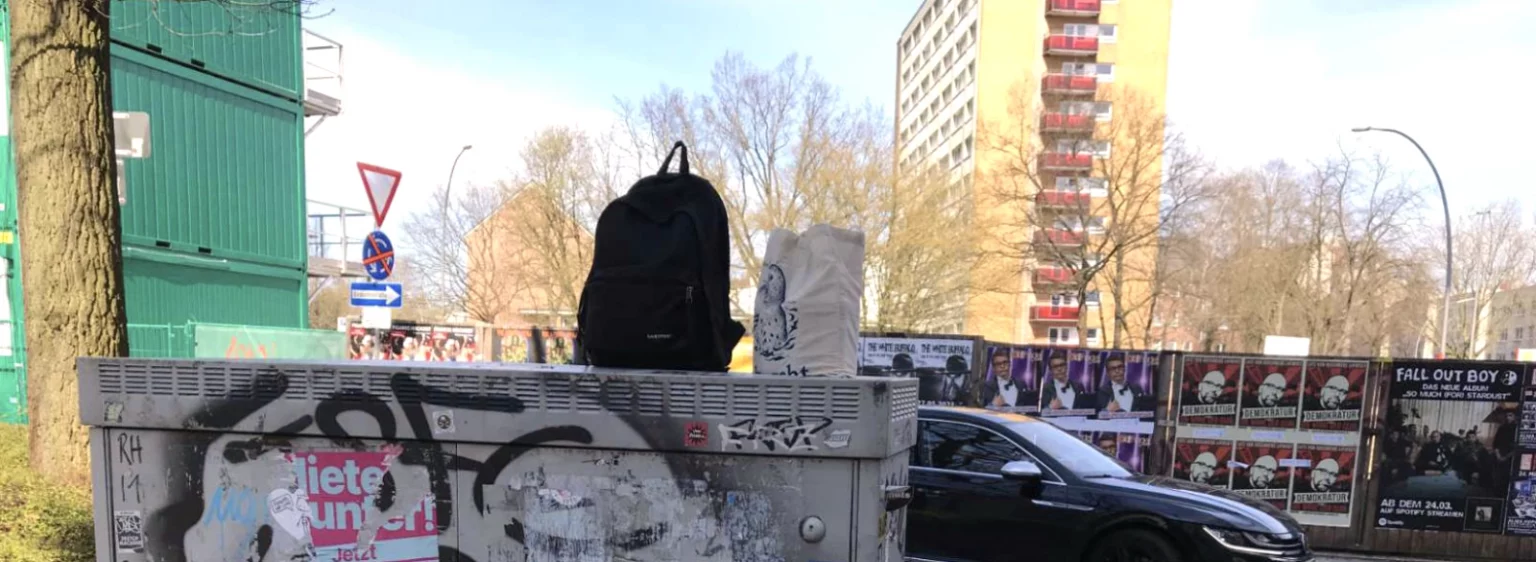 Rucksack und Stofftasche mit Sprühdosen auf unbemaltem Stromkasten.