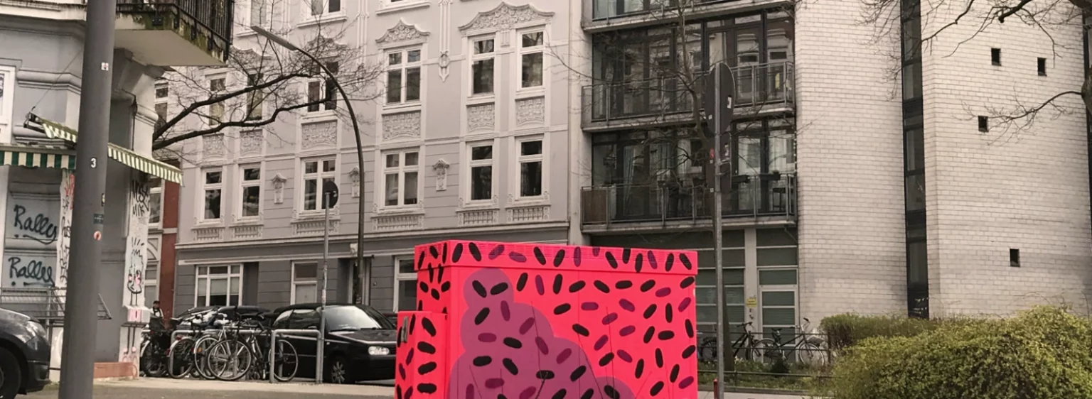 Fertiger Stromkasten von hinten vor grauer Hauswand, kräftige Farben im Kontrast.